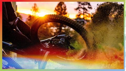 A mountain bikers back wheel during sunset slashing through a dirt berm